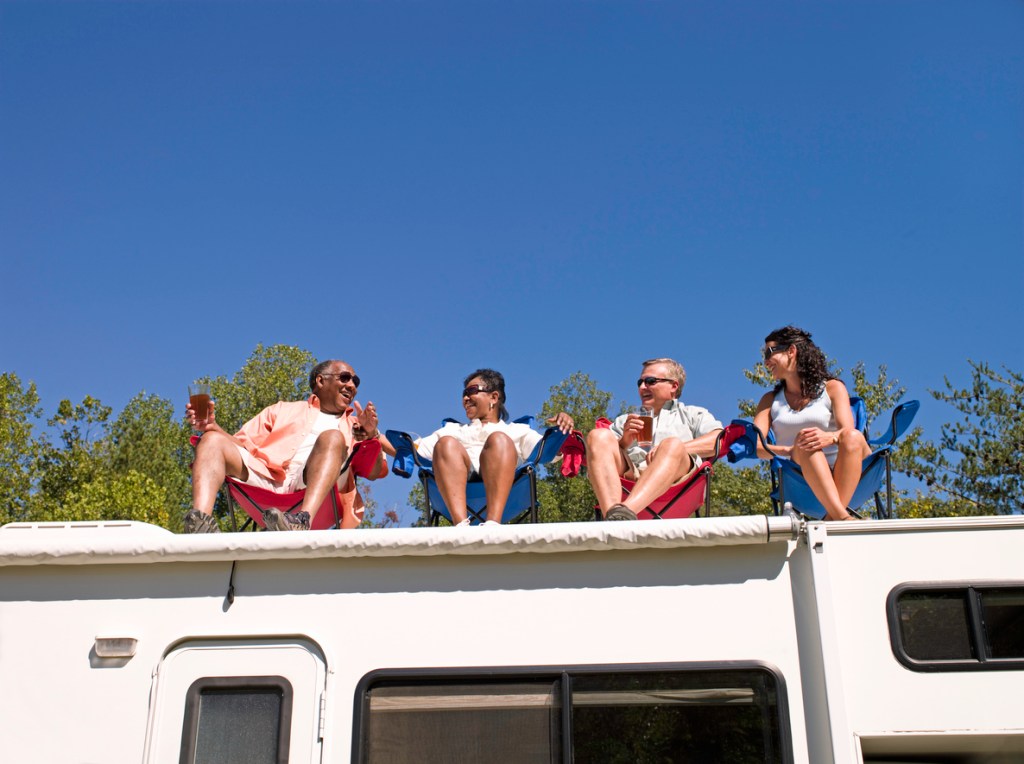Four people sitting in chairs on a RV roof, which made lead to the need for repairs.