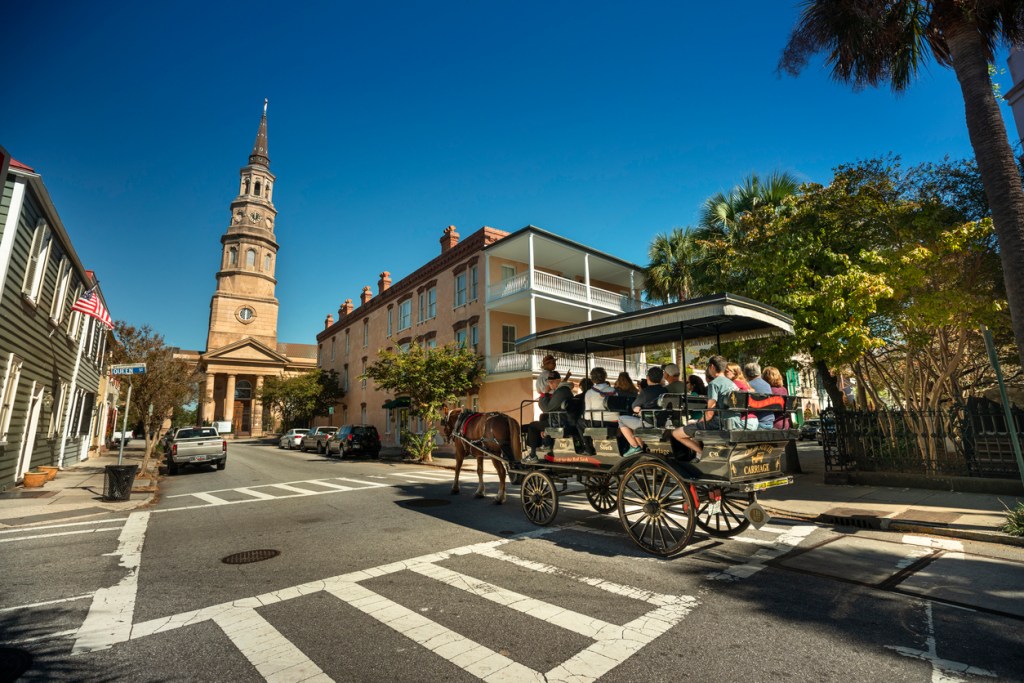 People take a carriage ride by St. Philip's Church in historic downtown Charleston South Carolina USA. Some of them may stop at a rooftop bar when they're done.