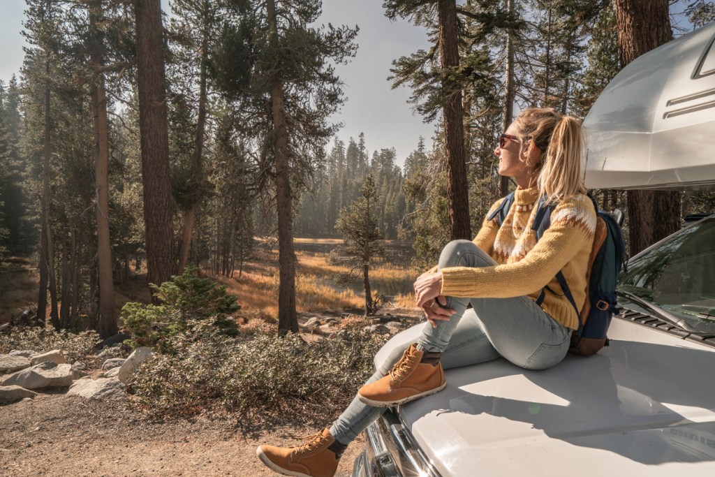 Woman on hood of an RV in the woods, enjoying her solo travels