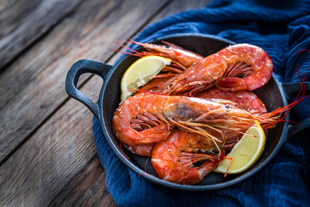 High angle view of fresh shrimps in a cast iron cooking pan shot on rustic wooden table. Gulf shrimp are extremely popular at dinner tables around the South.