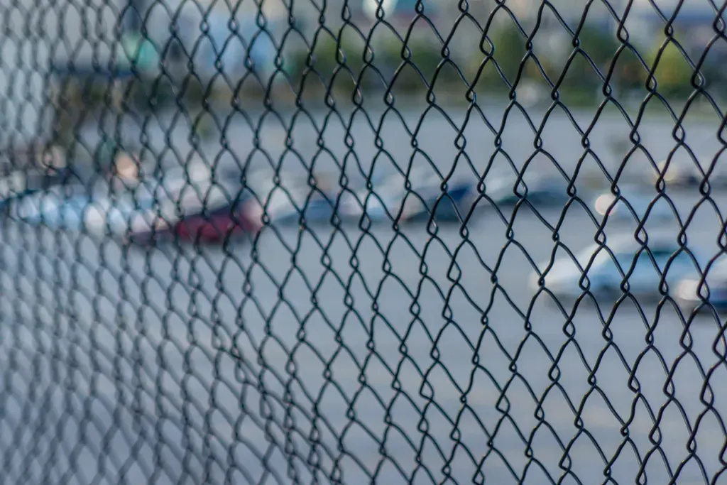 Close up of chain-link fence with what could be an impound lot with an RV in the background