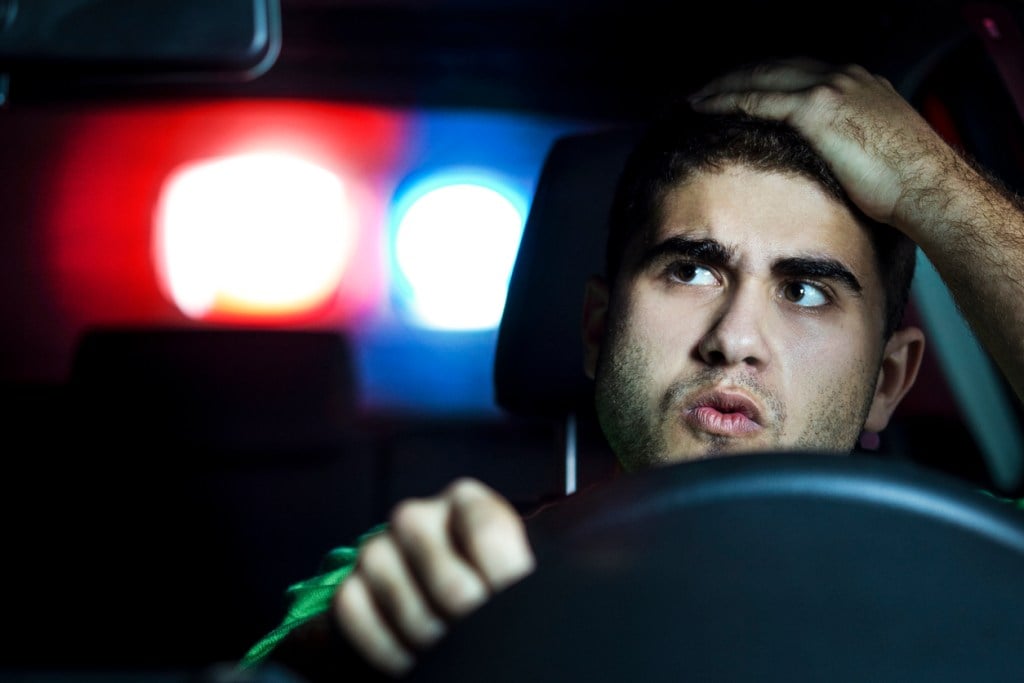 Police lights behind a man driving a car. Is he being pulled over for driving naked?