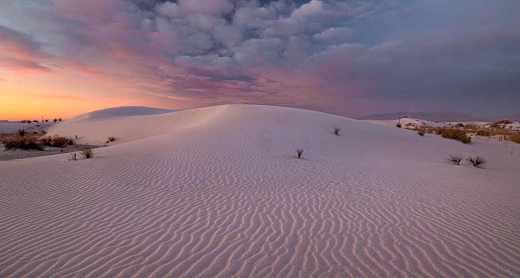 Beautiful sunrise with clouds and pink sky light up the sand dunes. Weather at White Sands National Park is one of the dangers.