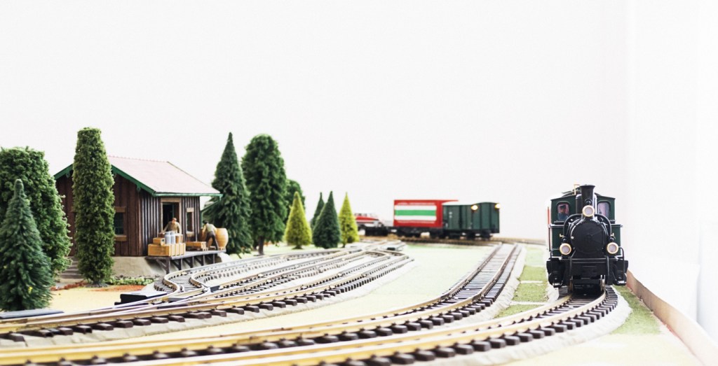 Model railway featuring agricultural siding and steam train, with workers preparing farm products. 