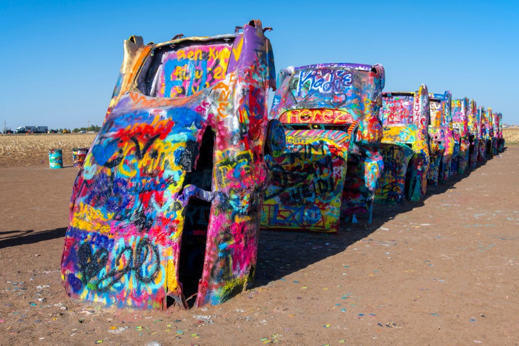 A row of half-buried cadillacs covered in graffiti at the Cadillac Ranch