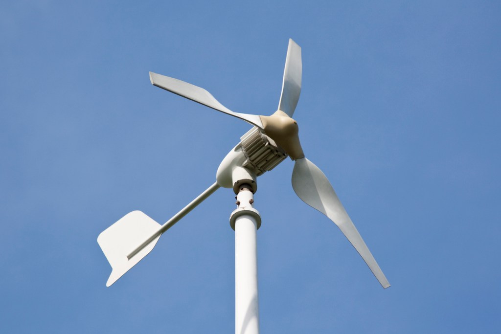 Small white wind turbine generator on pylon against blue sky.