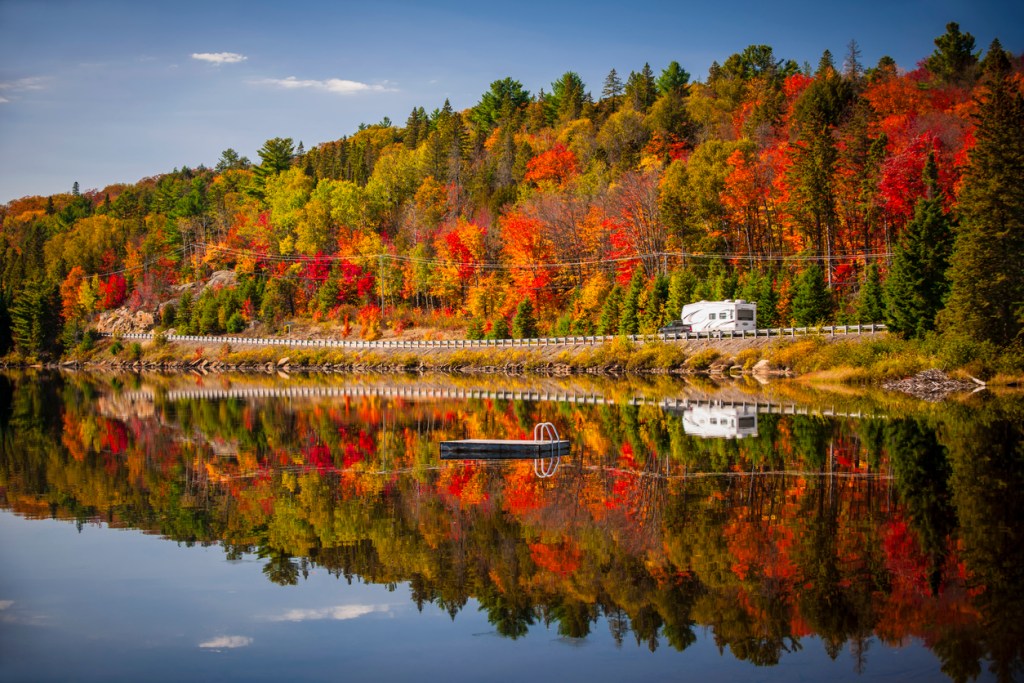 Fall forest with colorful autumn leaves and an RV parked along a lake