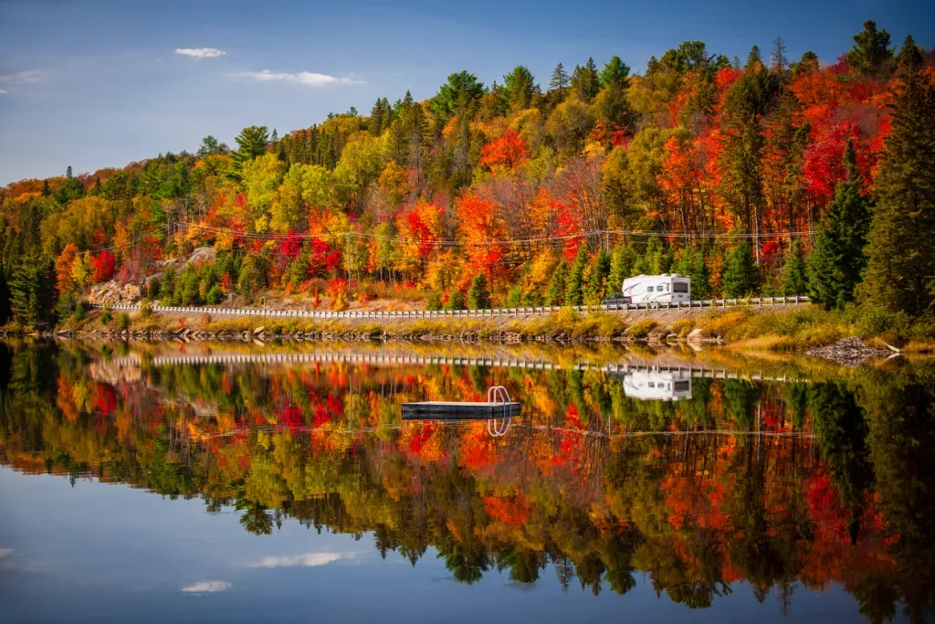 Fall forest with colorful autumn leaves and an RV parked along a lake