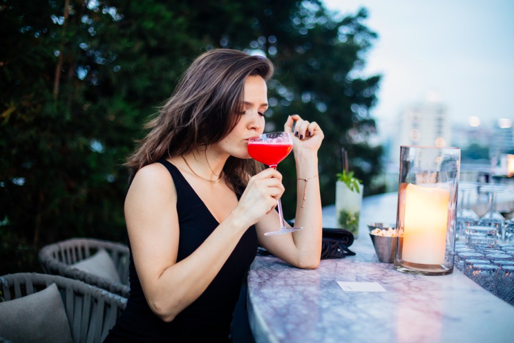 A woman drinking a pink cocktail at a rooftop bar