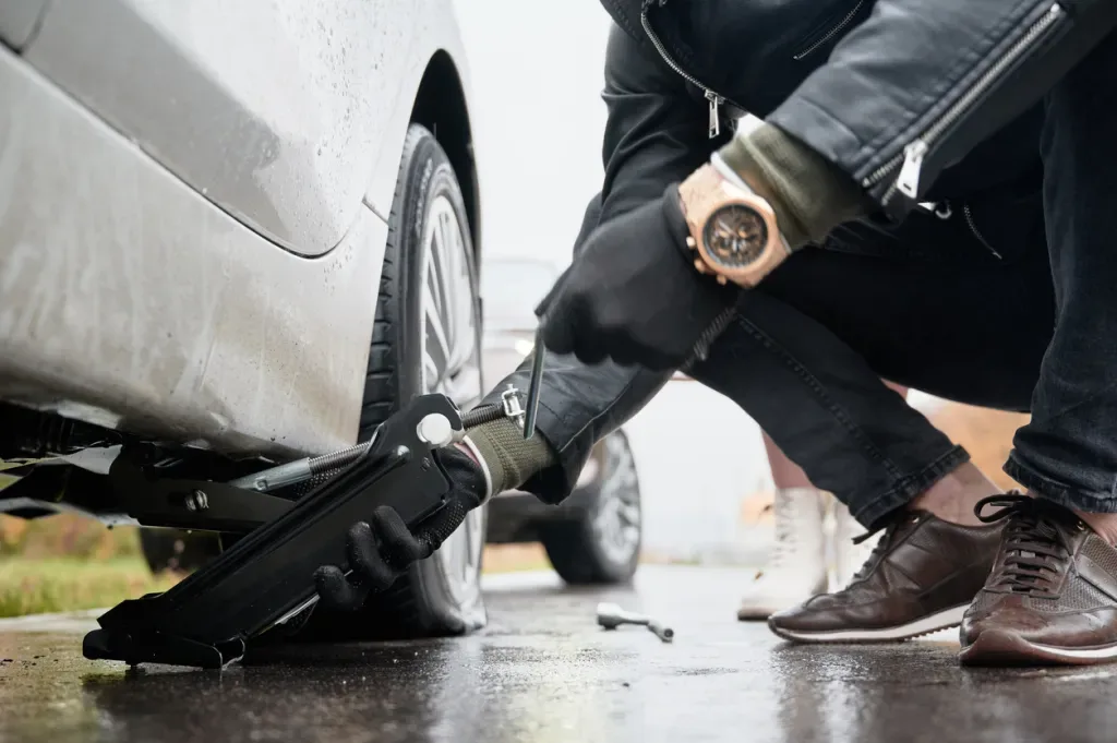 A person wearing black gloves lifts a car with a jack. Are they preparing to steal the catalytic converter?