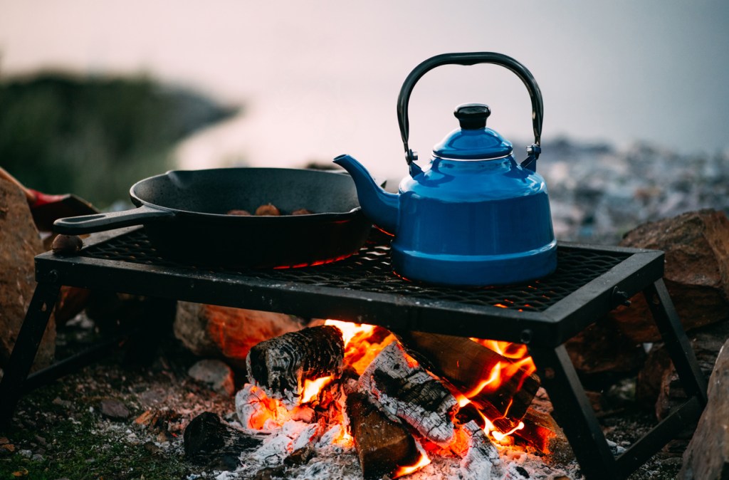Teapot and Cast Iron Skillet Over Campfire. Whether over the fire or on a stove, one pot camp meals win!