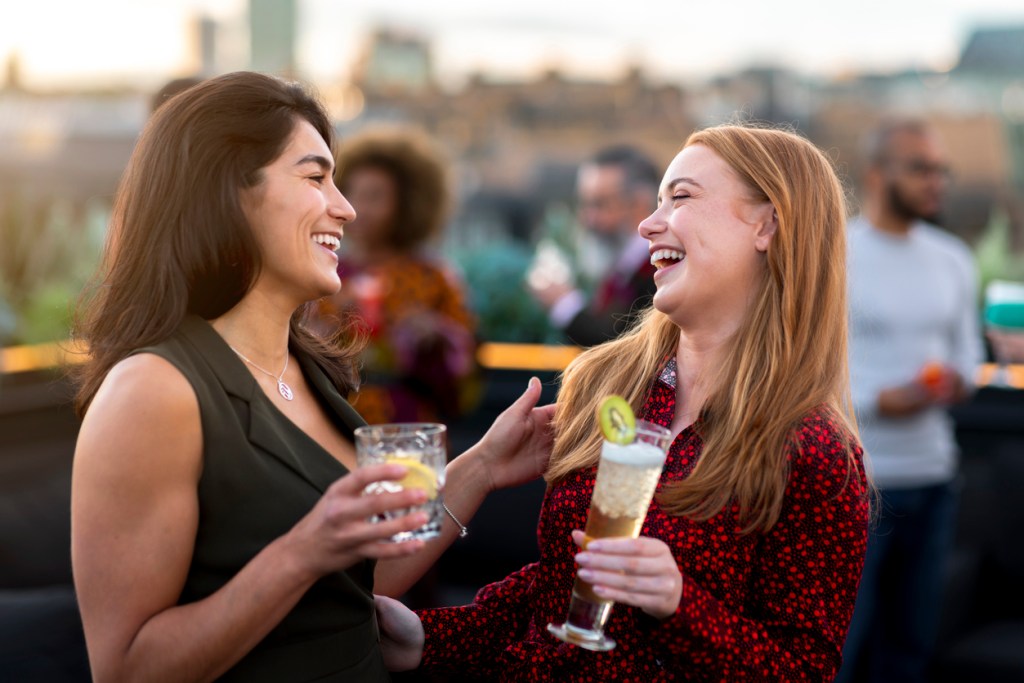 Two women laughing and having drinks on a rooftop bar similar to those you'll find in Savannah, Georgia.