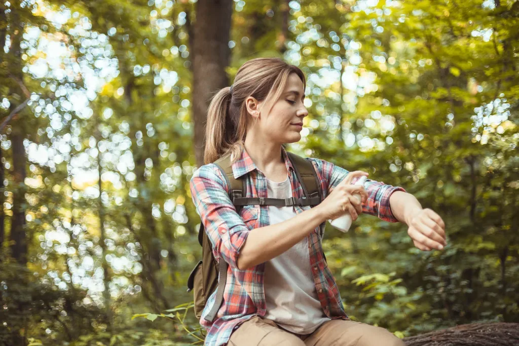 Woman Applying Insect Repellent Against Mosquito and Tick During Hike in Nature. Protect yourself against disease-carrying mosquitoes.