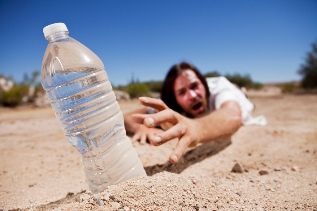Man crawling through the desert reaching for bottle of water. Dehydration is one of the dangers of soaking in hot springs.