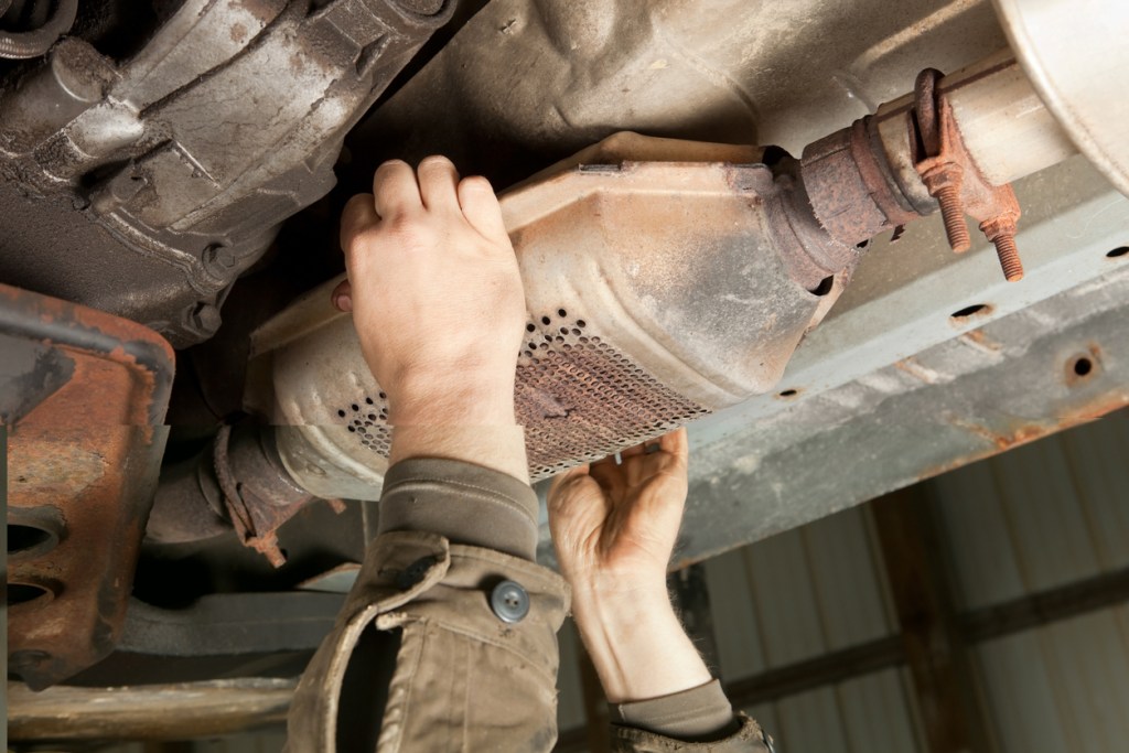 A man removing a catalytic converter from under a car