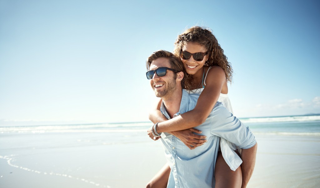 Shot of a young man giving a woman a piggyback ride on a beach, which is a common snowbird destination