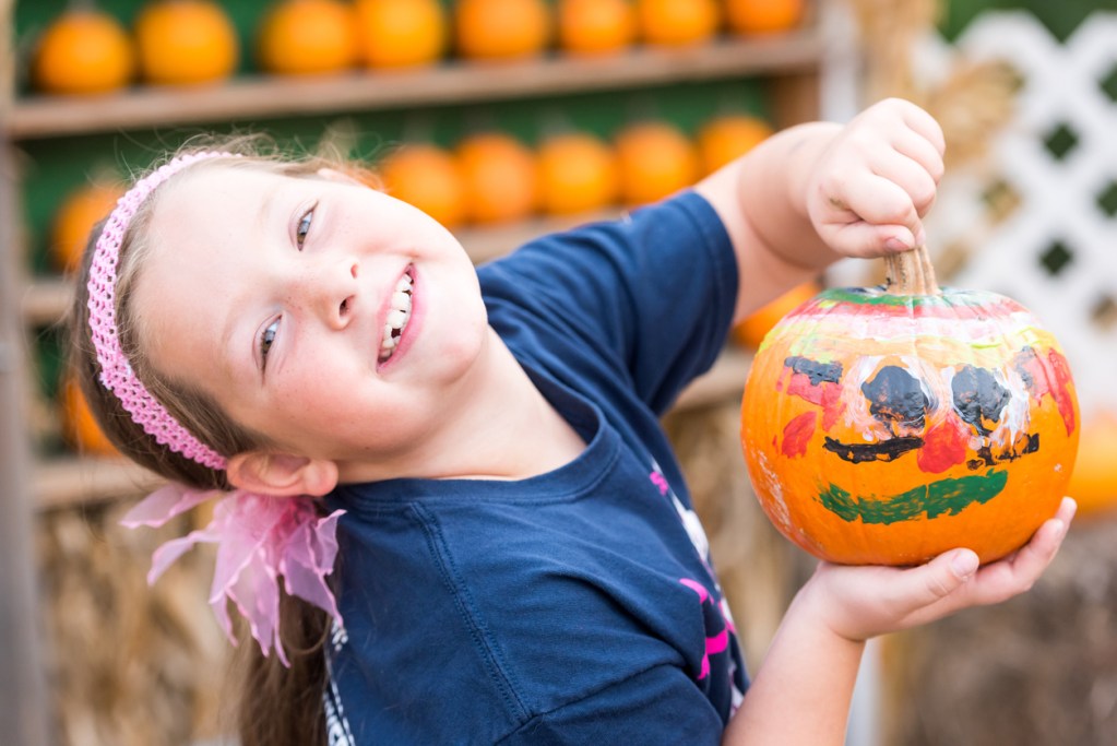 A young girl smiling and showing her painted pumpkin. Many RV parks offer Halloween activities for kids.