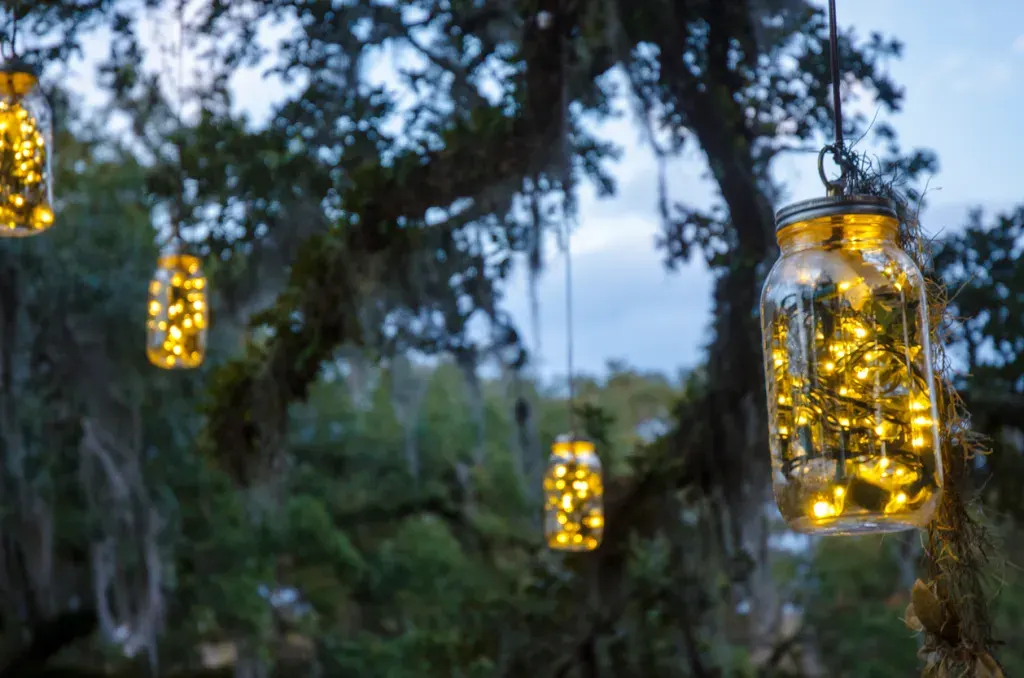 Glass Jars with Christmas Lights Hanging from Oak Trees have been decorated with white lights. The fireflies in a jar effect brings back childhood memories.
