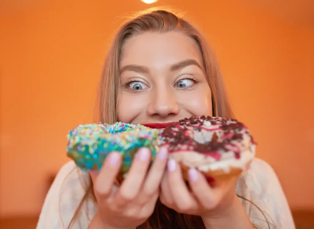 portrait of funny woman eating delicious doughnuts, looking with her eyes crossed.