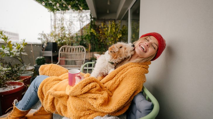 Photo of a young woman having a warm drink on a cold winter day while enjoying with her dog on her patio