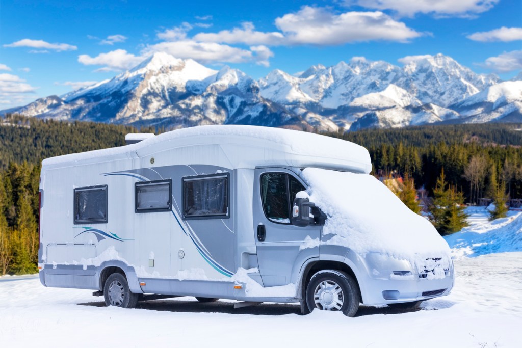 An RV covered in snow with mountains in the background. 