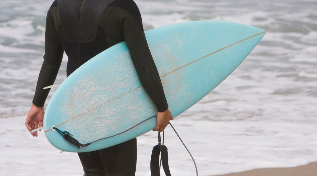 A surfer walking with a blue surfboard. Encinitas offers excellent waves and is an easy day trip from San Diego.