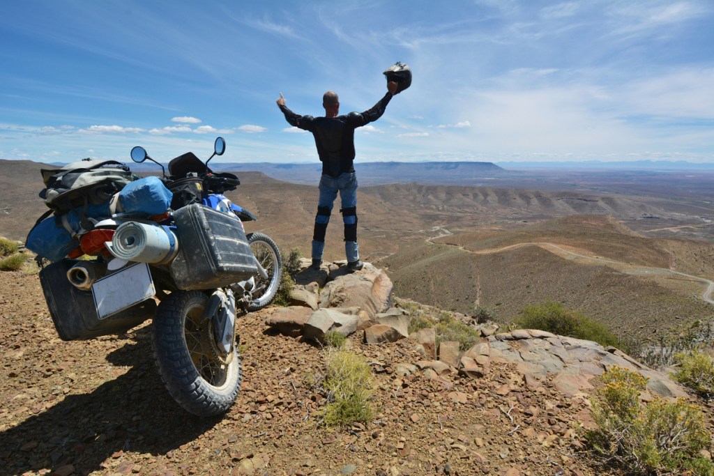 A motorcyclist stands next to his motorcycle and appreciates the view. Where could the Honda Transalp take you?