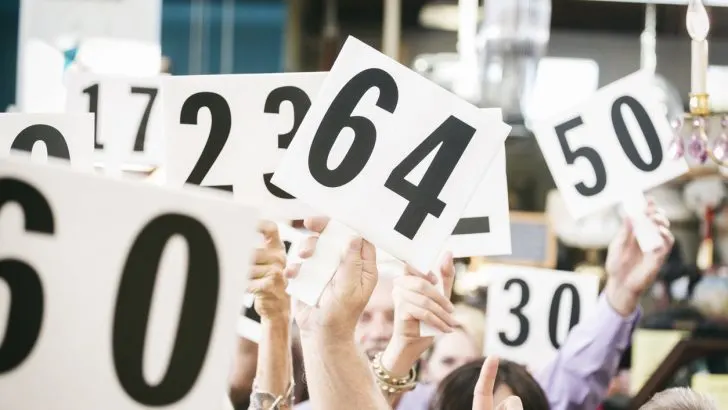 A crowd of bidders at an auction, holding their numbered bidding paddles in the air.