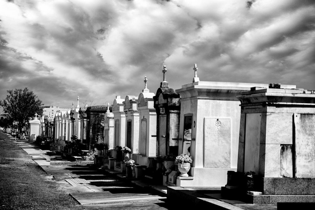 Creepy black and White shot of a row of mausoleums under a dramatic sky in New Orleans, Louisiana.