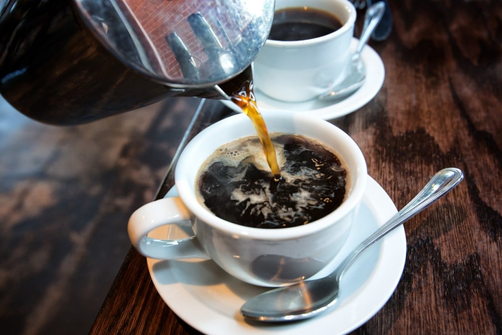 Fresh hot coffee being poured into a cup from a stainless steel French press in a trendy cafe, can coffee be considered a tea
