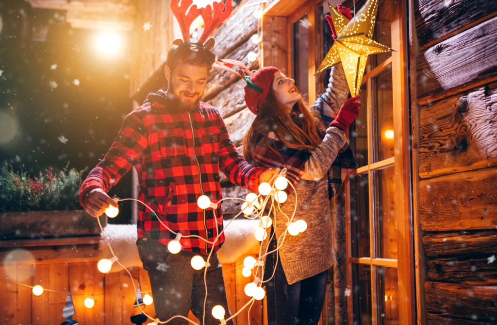 Couple decorating porch with string lights for Christmas. 