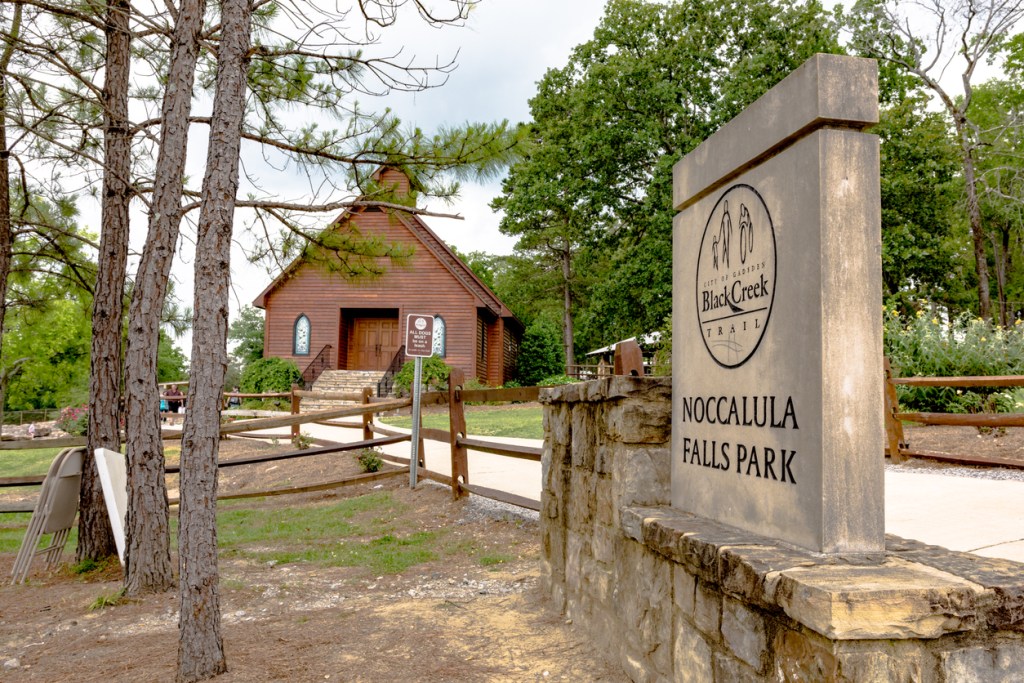 Noccalula Falls Park sign with wedding chapel in the background.