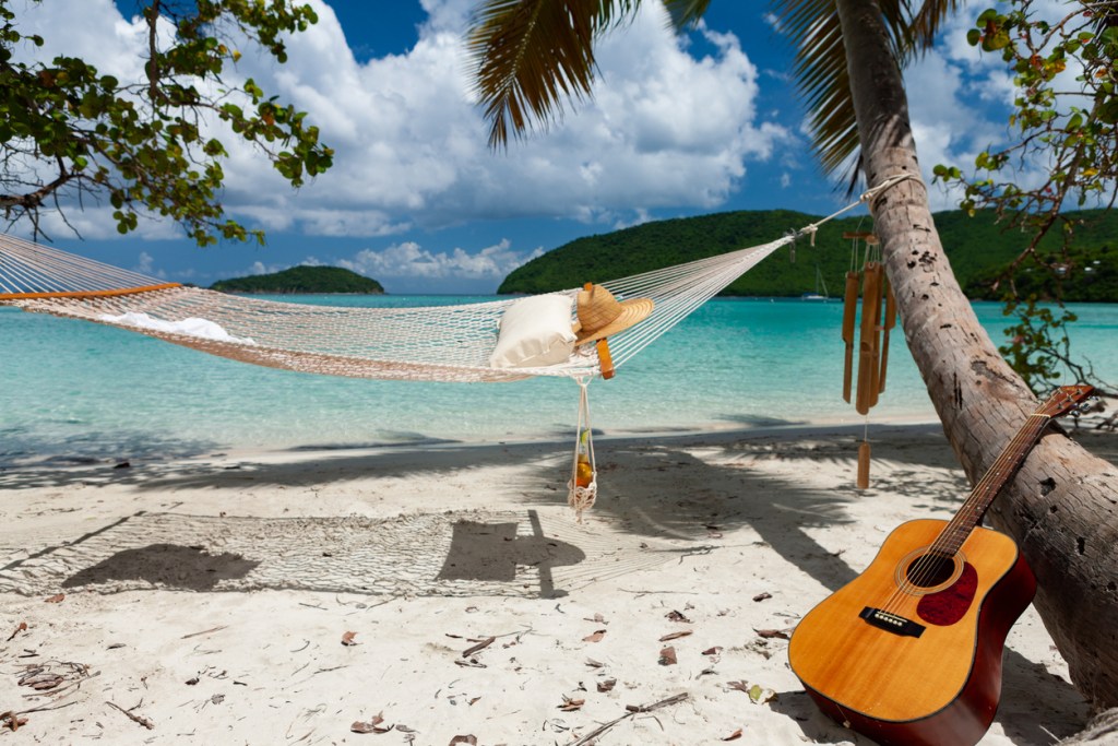 A guitar and hammock on a beach with palm trees, representing the music festivals in Key West