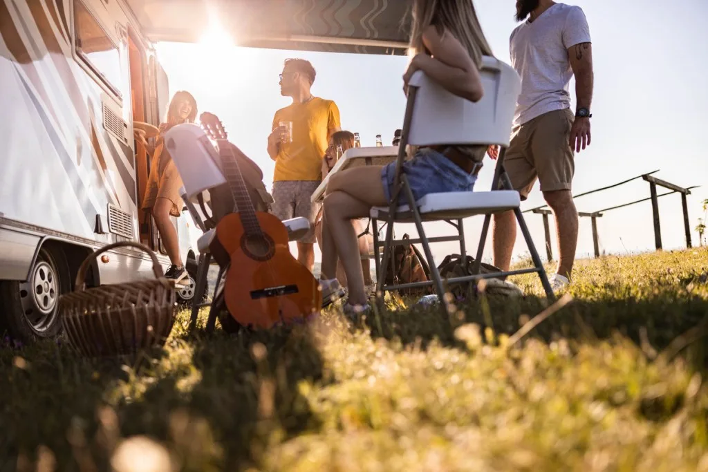 Low angle view of group of young happy friends talking while spending a spring day camping. What does the Grand Design micro camper look like?
