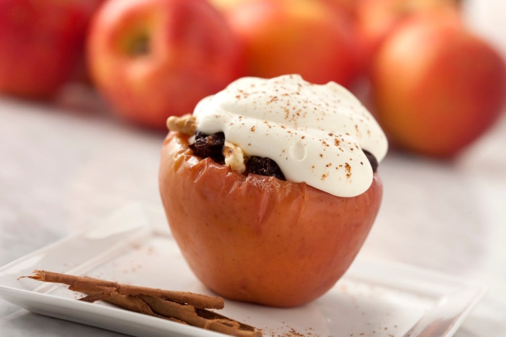 Baked apple stuffed with raisins and walnuts are a favorite holiday dessert. Cream and cinamon on top. Red apples on background.