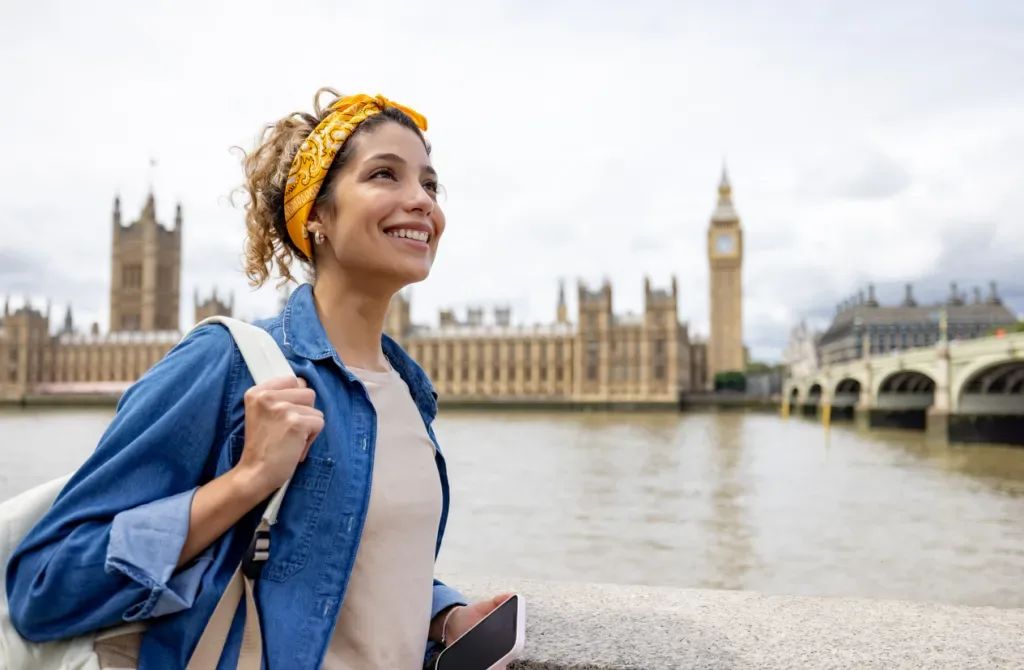 Happy woman sightseeing in London around the Big Ben. She may have gotten discount travel offers at a local trade show.