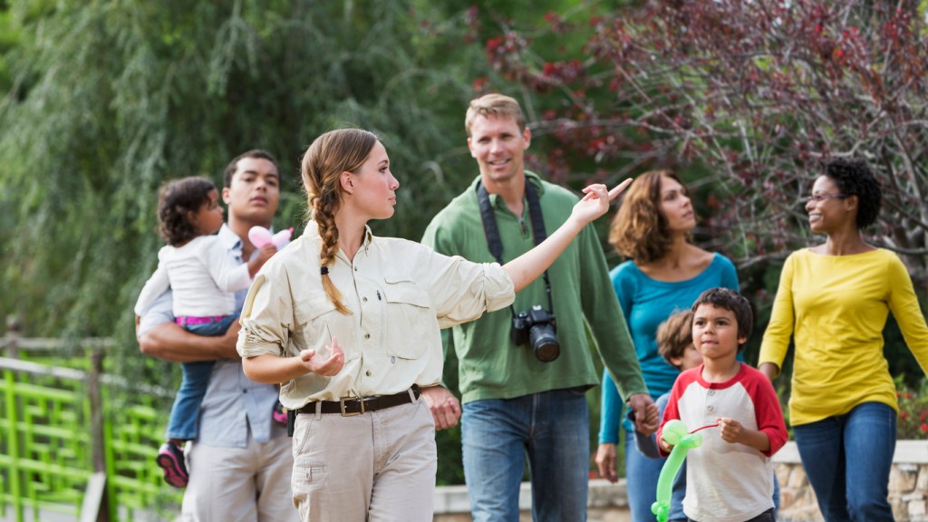 Tourists walking with tour guide in a park. Tour guides can work indoors or outdoors and is an excellent option for travel work.