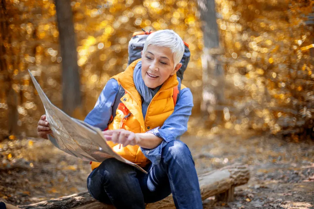 Woman reading a map in the forest. It's smarter to use paper topographical maps than Google Maps to avoid fake trails.