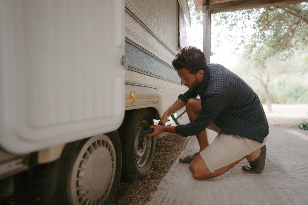 Photo of a man repairing wheels of his recreational vehicle. Maybe he should have been using tire covers.