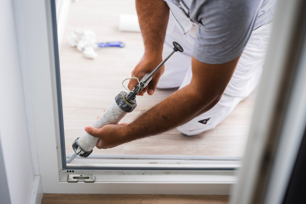A construction worker using sealant on a sliding glass door