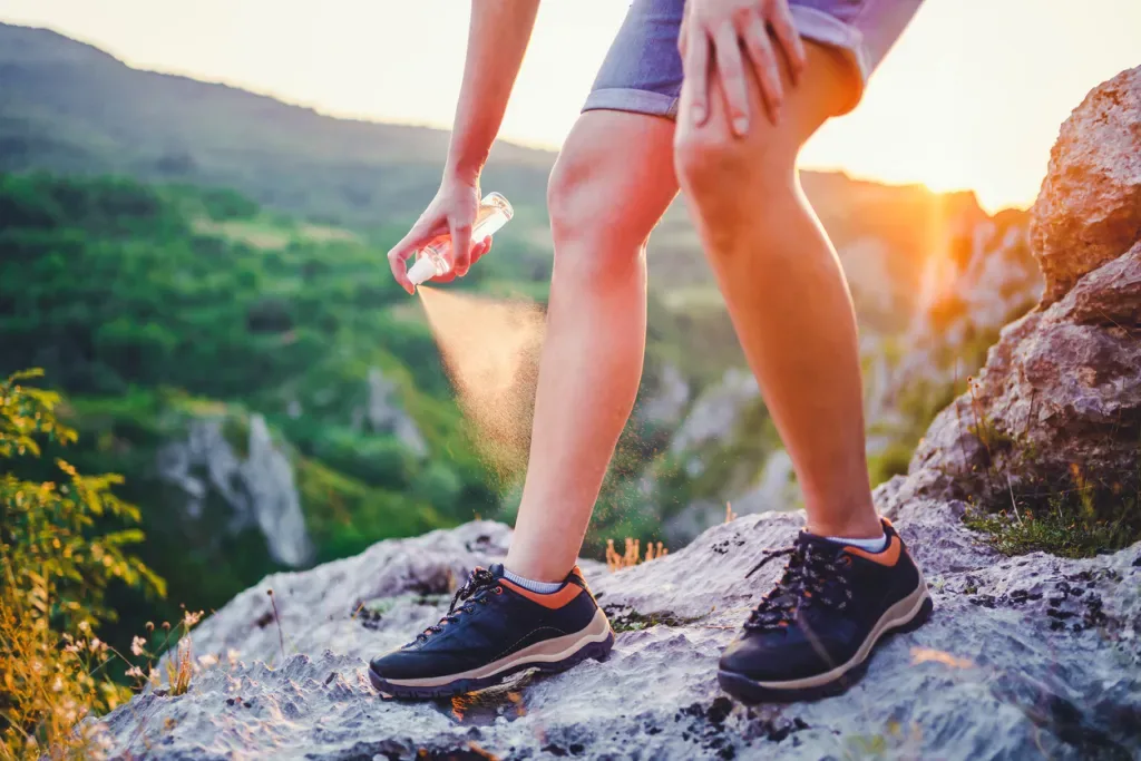 Hiker applies bug spray to their legs on a rocky outcropping, perhaps to fend off this deadly tick disease.