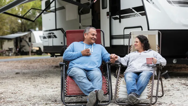 A man and woman sitting in front of their RV on a lot