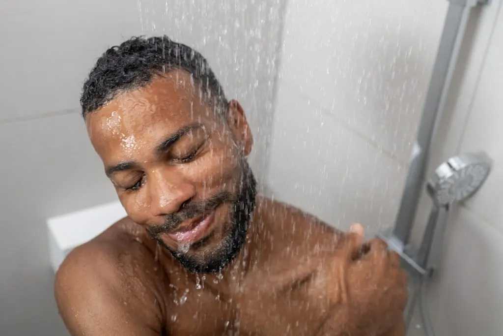 Smiling man with eyes closed taking shower in bathroom. The shower head could be an inexpensive one.