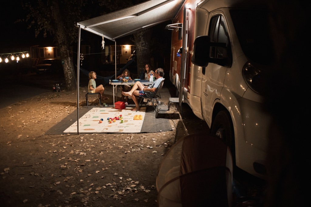 Happy family talking at a picnic table by the camper trailer in nature at night. Seasonal campgrounds offer you the chance to settle into your space.