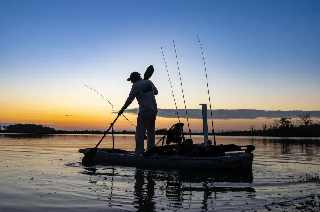 A man paddles a small boat with several fishing rods on board.