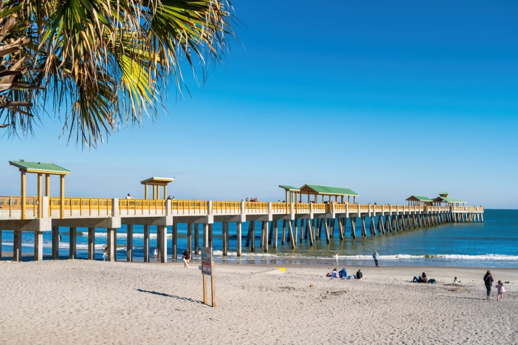 A pier extends out over the ocean, similar to what you'd see at a South Carolina State Park.