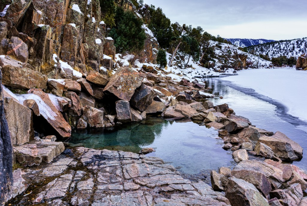Welcoming hot springs surrounded by snow-capped rocks and distant mountains.