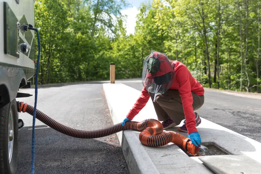 Person in a red jacket emptying RV sewage at a dump station. You'll want a cheap holding tank treatment before releasing your waste!