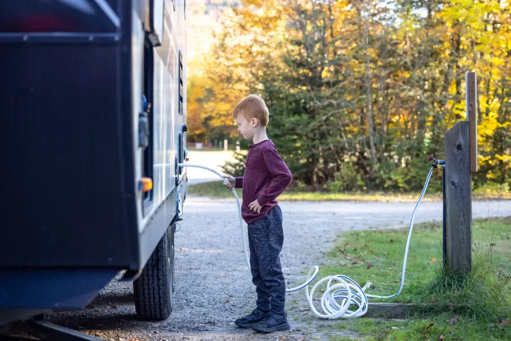 A young boy uses a cheap freshwater hose to fill an RV tank.