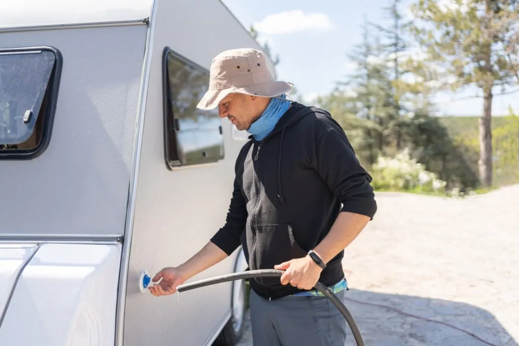 A man fills up his RV's freshwater tank with a cheap hose.